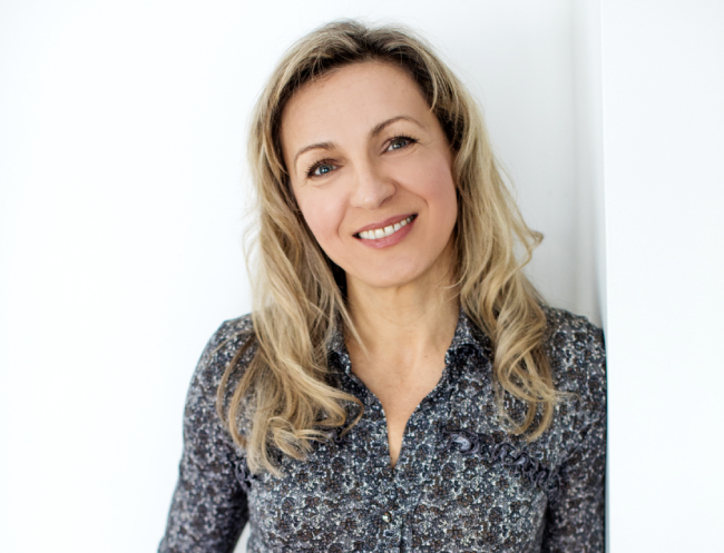 Smiling woman, Renata the founder and owner of Pearly Whites for Pets, with long blonde hair wearing a patterned shirt, representing expertise in pet teeth cleaning services at Pearly Whites for Pets.